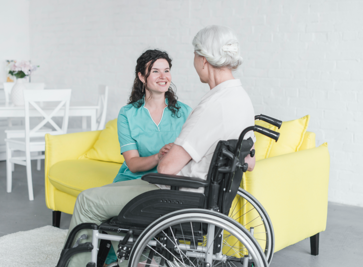 smiling-woman-looking-senior-woman-sitting-wheel-chair@2x